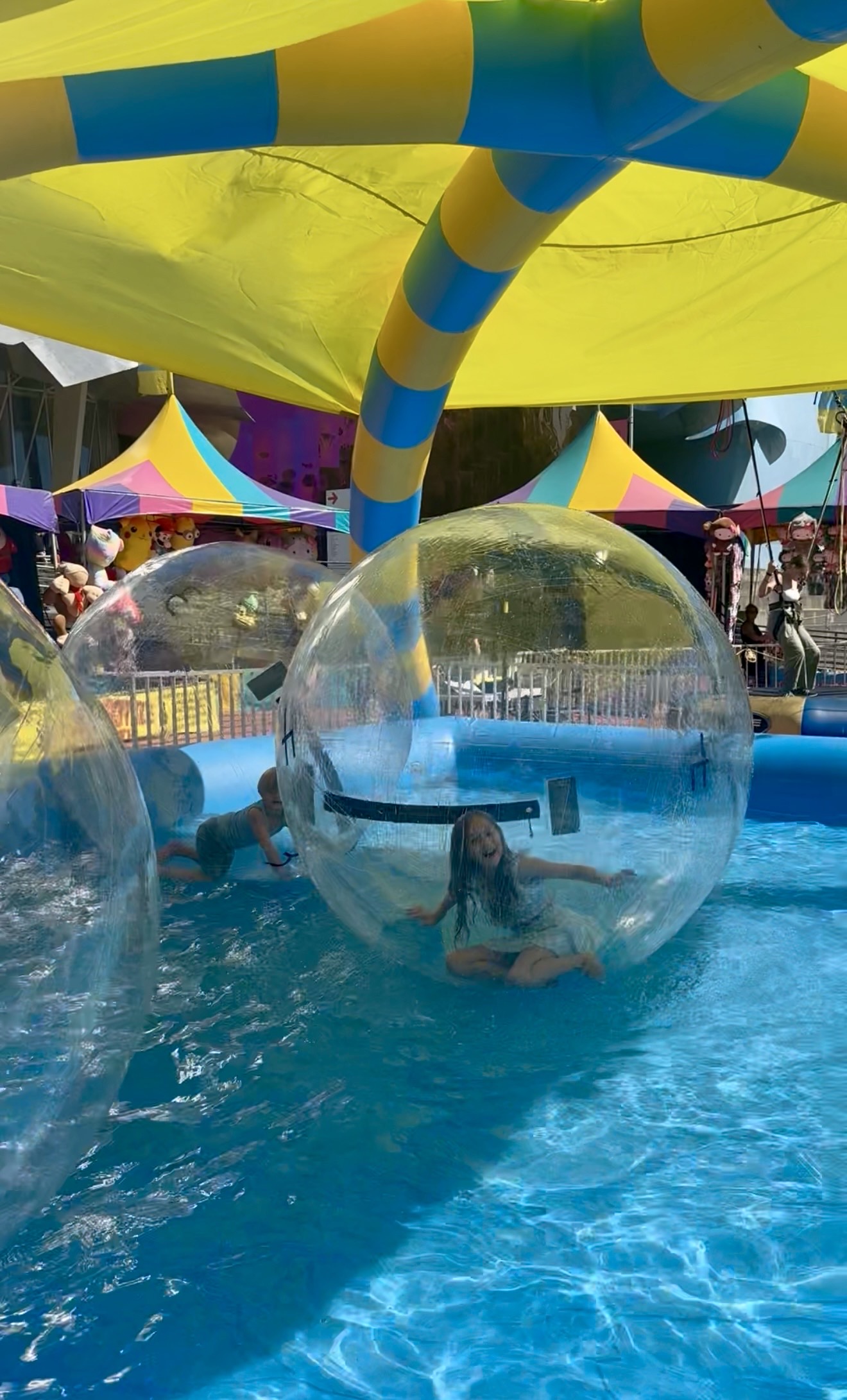 Girl smiling inside a water walking ball surrounded by blue pool water